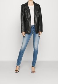 Mustat nahkablazerit, joissa on viistetyt liepeet ja kaksi etutaskua, yhdistettynä vaaleansinisiin kuluneisiin skinny-farkkuihin ja mustiin korkokenkiin.