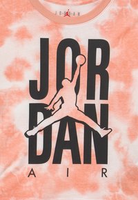 Orange tie-dye t-shirt med en stor svart "JORDAN" grafik och silhuett av en hoppande figur. Tillverkad av bomull med rund halsringning.
