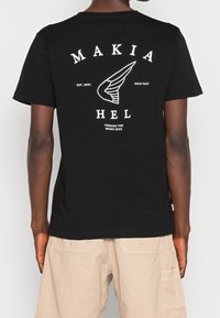 T-shirt en coton noir avec un graphisme blanc comportant du texte et un motif d'ailes au dos, manches courtes et col rond.