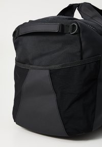 Sac à dos noir en nylon texturé et maille, avec une forme arrondie, une poche latérale et une poignée de transport sur le dessus.