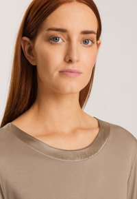 Beige topp med en mjuk satin krage, mjuk textur och en avslappnad passform. Designen har en enkel, elegant form på kragen.