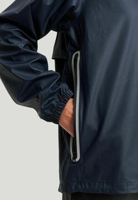 Mørkeblå vandtæt jakke med elastiske manchetter og en lynlåslomme med grå detaljer. Glat tekstur og moderne design.