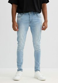 Vaqueros de denim azul claro con un corte ajustado, que presentan un diseño clásico de cinco bolsillos y un leve efecto de desgaste, combinados con zapatillas blancas.