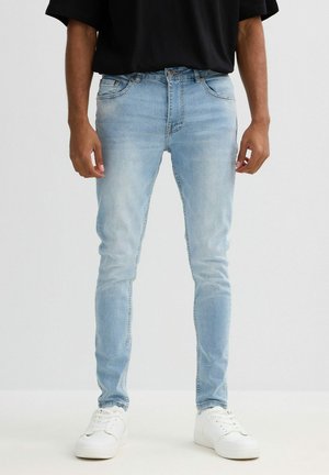 Vaqueros de denim azul claro con un corte ajustado, que presentan un diseño clásico de cinco bolsillos y un leve efecto de desgaste, combinados con zapatillas blancas.