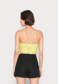 Top amarelo cropped com fecho de correr nas costas, combinado com calções pretos de cintura alta. Design simples, textura suave, sem padrões.