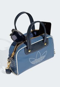 Blue handbag with perforated leather details, short handles, gold zipper, and a logo patch. Contains sunglasses and a smartphone inside.