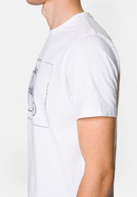 Biała bawełniana koszulka z nadrukiem na przodzie. Krótkie rękawy i klasyczny okrągły dekolt. Gładka faktura i luźny krój.