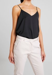 Camisole en satin noir avec un décolleté en V et des fines bretelles, associée à un pantalon texturé beige clair avec des poches latérales.