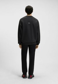 Czarny sweter z okrągłym dekoltem, ściągacze przy mankietach i dolnym brzegu, noszony z czarnymi spodniami i ciemnymi butami z czerwonymi akcentami, minimalistyczny design.