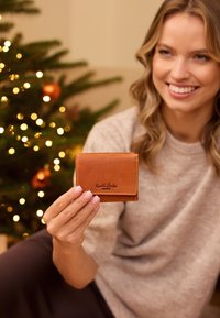 Brown leather wallet with a fold design, featuring a stitched trim and embossed logo. The surface has a smooth texture.