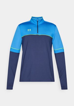 T-shirt de sport à manches longues avec un col zippé mi-hauteur. Blocs de couleur bleu et marine avec des accents verts. Tissu lisse, coupe athlétique. Logo Under Armour visible.