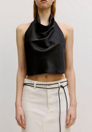 Zwarte, mouwloze cropped top van gladde, gedrapeerde stof met een kraag; gecombineerd met een witte denimrok met hoge taille en riem.