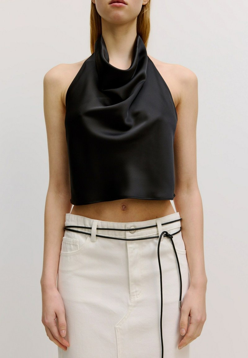 Zwarte, mouwloze cropped top van gladde, gedrapeerde stof met een kraag; gecombineerd met een witte denimrok met hoge taille en riem.