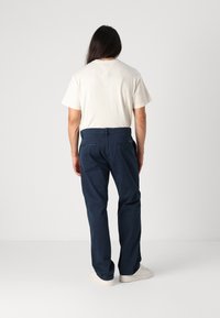 Béžová košile s krátkými rukávy spojená s tmavě modrými, volnými kalhotami. Kalhoty mají zadní kapsy a hladkou strukturu. Bílé tenisky.