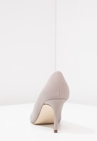 Grauer High Heel-Schuh mit einem strukturierten synthetischen Obermaterial, spitzem Zehenbereich und einem schlanken, braunen Akzent-Absatz, vor einem weißen Hintergrund.