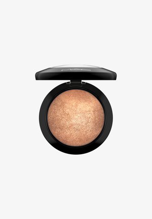 Compact de surligneur MAC rond avec un extérieur noir ; comprend un produit bronze scintillant à l'intérieur, présentant une surface lisse et texturée.