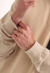 Sudadera beige con puños acanalados, que presenta una textura suave y un corte relajado. Los puños están ligeramente doblados, revelando la tela de debajo.