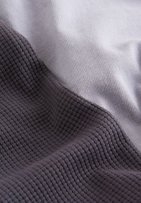 Kahemõõtmeline vaade kahe tekstuuriga kangalapi lähedalt, üks helehall ja teine tumehall, näidates kudumismustreid ja pehmeid voldikuid.