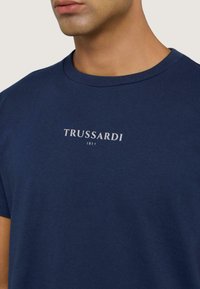 Camiseta de color azul marino hecha de algodón con cuello redondo, que presenta un logo blanco de "TRUSSARDI 1911" impreso en el pecho.