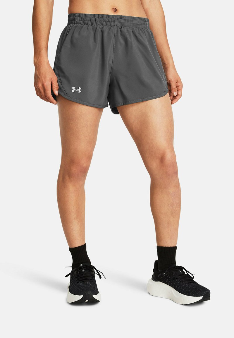Graue sportliche Shorts mit einem elastischen Bund und Seitentaschen. Mit Logo am linken Saum. Getragen mit schwarzen Schuhen und Socken.