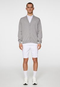 Ljusgrå cardigan i mjukt stickat material med V-hals, knappfram och ribbade ärmar, tillsammans med vita shorts och sneakers.