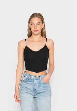 Top crop preto com renda, alças ajustáveis e bainha em formato escalope. Usado com jeans de cintura alta desgastados em azul claro.
