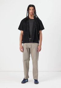 Black short-sleeve button-up shirt over a dark gray t-shirt, paired with light khaki pants and navy sneakers with white stripes.