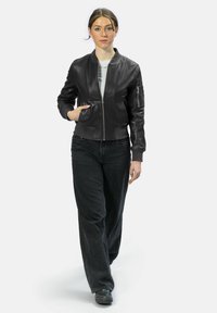 Schwarze Lederbomberjacke mit gerippten Bündchen und Saum, Reißverschluss vorne, Seitentaschen und einer zusätzlichen Tasche am linken Ärmel.