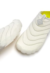 Weiße Slipper mit einem strukturierten, gesteppten Muster und einer semi-transparenten Gummisohle. Mit einem grauen Akzent oben und kleinen Punkten.