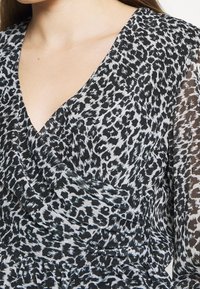Robe à imprimé léopard noir et blanc avec un col en V, un corsage drapé et des manches longues transparentes. Tissu texturé avec un design fluide.