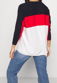 Stickad tröja med en färgblockdesign som har en marinblå överdel, en röd mittstripe och botten i vitt. Avslappnad passform med trekvartslånga ärmar.