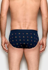 Plavky v námořnicky modré barvě s přiléhavým střihem, zdobené opakujícím se vzorem perníkových panáčků a červenými akcenty, vyrobené z hladké látky.