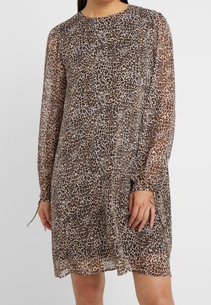 Femme portant une robe à manches longues, longueur genoux, avec un motif léopard marron et noir.