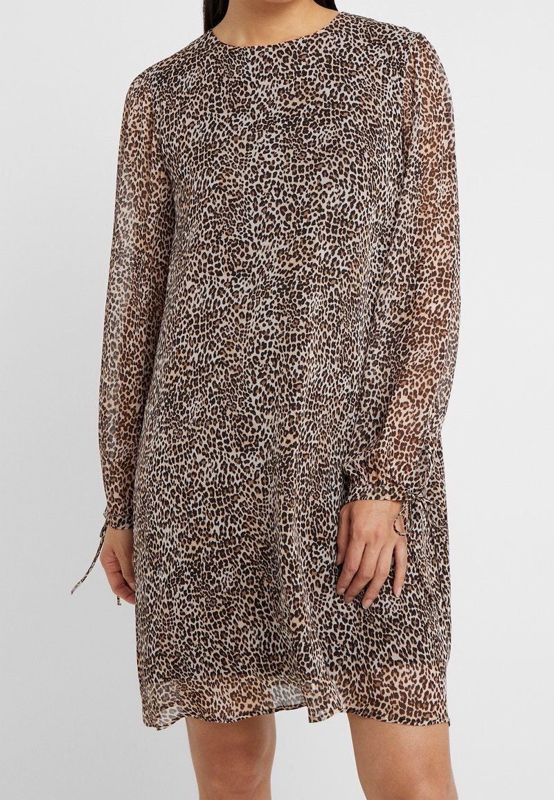 Femme portant une robe à manches longues, longueur genoux, avec un motif léopard marron et noir.