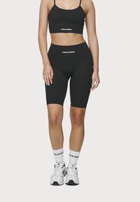 Zwarte crop top en hoge fietsbroek van rekbare stof. Witte merkl logo op beide. Gemaakt met witte sneakers en crew sokken.