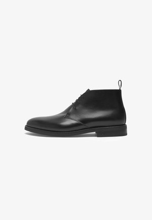 Stivali alla caviglia in pelle nera con finitura liscia, punta rotonda, lacci a due fori e un tirante sul tallone; suola piatta in gomma, design minimal.