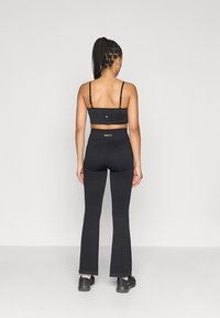 Μαύρο αθλητικό σουτιέν με λεπτές τιράντες και εφαρμοστή σχεδίαση, συνδυασμένο με μαύρο ψηλόμεσο κολάν με καμπάνες και υφή υφάσματος.