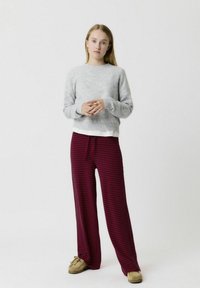 Un pull gris à col rond, associé à un pantalon large rayé rouge. La tenue présente une coupe décontractée et des textures douces. Des chaussures brunes à enfiler.