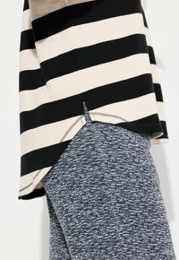 Top a strisce nere e crema con spacco laterale, abbinato a leggings blu con texture. Presenta una vestibilità rilassata e tessuti a contrasto.