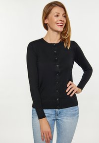 Mustan neulecardiganin pyöreä pääntie, pitkät hihat ja etunapit. Varustettu ribbausläpillä ja muotoonommellulla designilla.