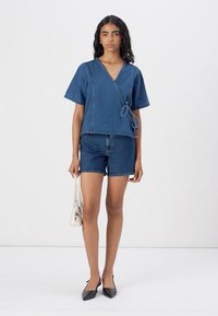 Top de denim com mangas curtas e laço lateral, combinado com calções de denim. O conjunto apresenta uma cor azul consistente e um design clássico.