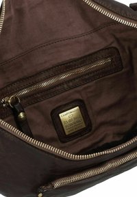 Binnenkant van een bruine leren tas met een donkere stofvoering, voorzien van een ritsvak, hardware-accenten en een gouden label met "Campomaggi."