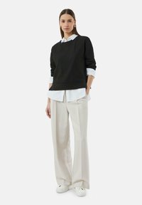 Black ribbed sweater layered over a white button-up shirt, paired with cream wide-leg trousers and white sneakers. Minimalist design.