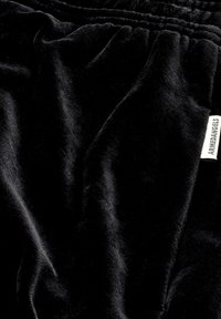 Nahaufnahme von schwarzem, samtigem Stoff mit gerafftem elastischen Bund und kleinem weißen Etikett, auf dem auf der rechten Seite "ARMAEDANGELS" steht.