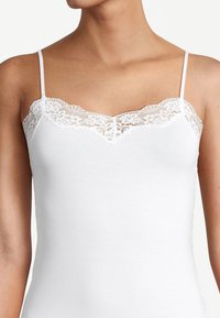 White camisole with thin straps, featuring a delicate lace trim along the neckline. Smooth texture, fitted design, and v-shaped cut.