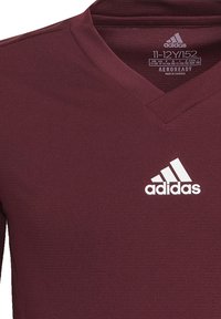 Bordeauxfarbenes Adidas Sportshirt mit V-Ausschnitt, gefertigt aus AEROREADY-Material; verfügt über ein weißes Adidas-Logo auf der Brust.