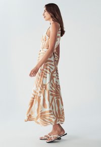 Maksi obleka v smetanasti barvi z velikimi bež vzorci listov, ki ima prilegajoč bodice, široke naramnice in zavezo v pasu. Uživana s črnimi sandali.