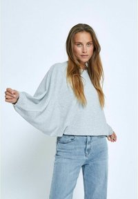 Helle graue Pullover mit strukturierten, oversized Ärmeln und einem weiten Halsausschnitt, kombiniert mit hellblauen Jeans. Weicher, lässiger Stoff.