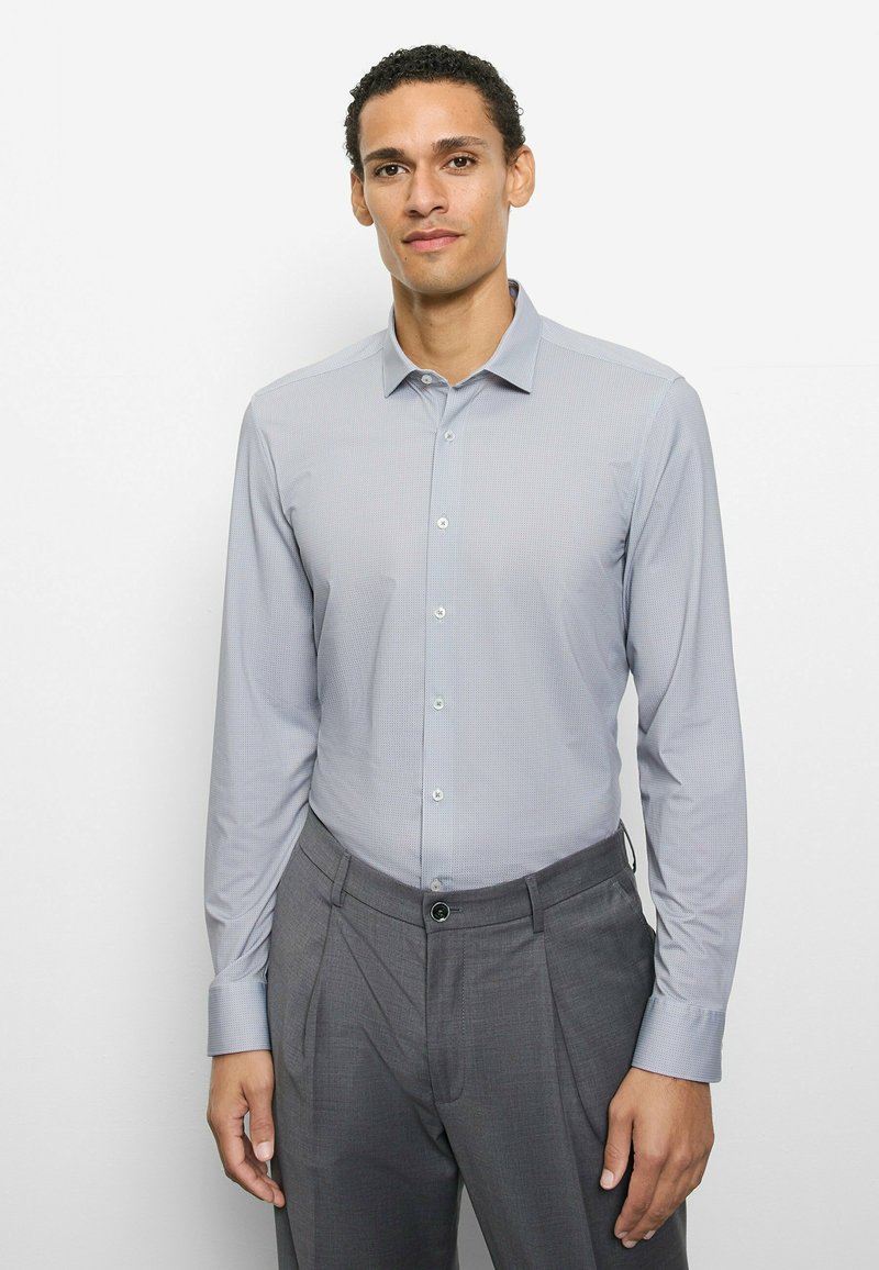 Hellgraues, langärmliges Hemd mit feinem Karomuster, Button-Down-Kragen und glattem Stoff, kombiniert mit dunkelgrauen Hosen.