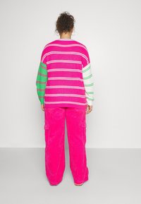 Flerfärgad tröja med rosa, grön och vit rand, kombinerad med ljusrosa kordbyxor med sidofickor.